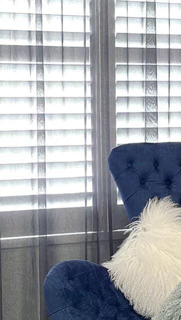 A stylish living room with floor-to-ceiling white curtains and a blue couch.