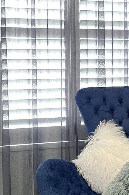 A stylish living room with floor-to-ceiling white curtains and a blue couch.
