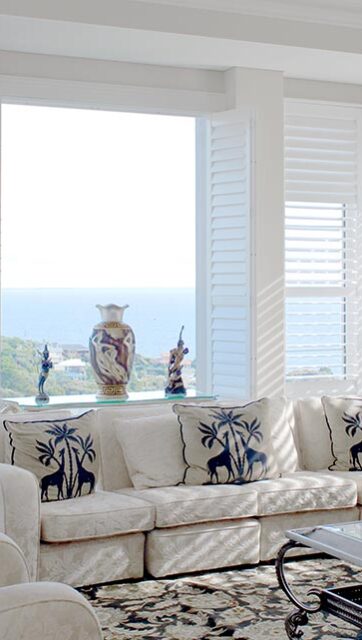 A bright and airy room with large windows, there are plants and furniture visible in the background.