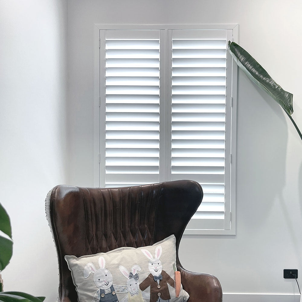 An image featuring the interior of a living room with large windows covered by white plantation shutters.