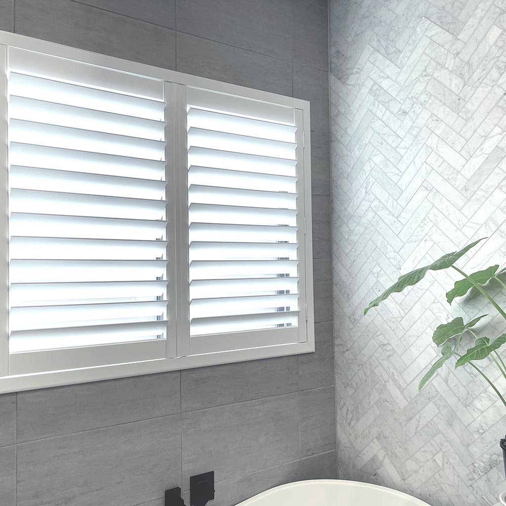 An image featuring the interior of a living room with large windows covered by white plantation shutters.