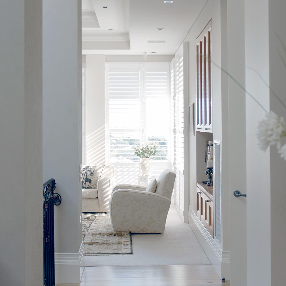 An image featuring the interior of a living room with large windows covered by white plantation shutters.