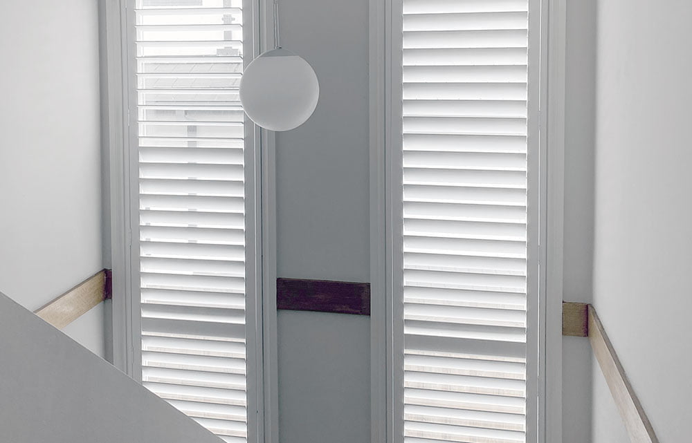 an image of a living room with a large window covered by white Basswood shutters.